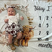 Blakely is registered to the contest to win money with this photo: age_marker, animal_illustration, baby, blanket, boots, celebration, child, clothing, cow_print, cute, decorative, floral, happy, headband, indoor, infant, lying_down, months, portrait, smiling