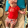 Blakely joined the competition — help win amazing prizes! baby, infant, child, bow, headwear, red_shirt, text_on_clothing, floral_shorts, socks, bed, pillow, blanket, indoor, person, cute, relaxed, lying_down, colorful, soft_toys, sleepwear