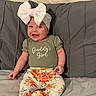 baby, child, smiling, headband, bow, green_shirt, floral_pants, sitting, bed, pillow, wooden_wall, happy, infant, cute, indoors, portrait, clothing, person, young_child, baby_girl
