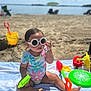 Raiden is registered to the contest to win money with this photo: toddler, beach, sunglasses, swimsuit, sand, towel, toy, shovel, bucket, frisbee, water, sunny, outdoor, child, play, summer, vacation, sitting, cute, colorful
