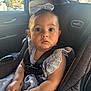 baby, child, car_seat, car_interior, seatbelt, bow, dress, lace, striped, person, infant, sitting, hands, face, eyes, window, door, adult, vehicle, safety