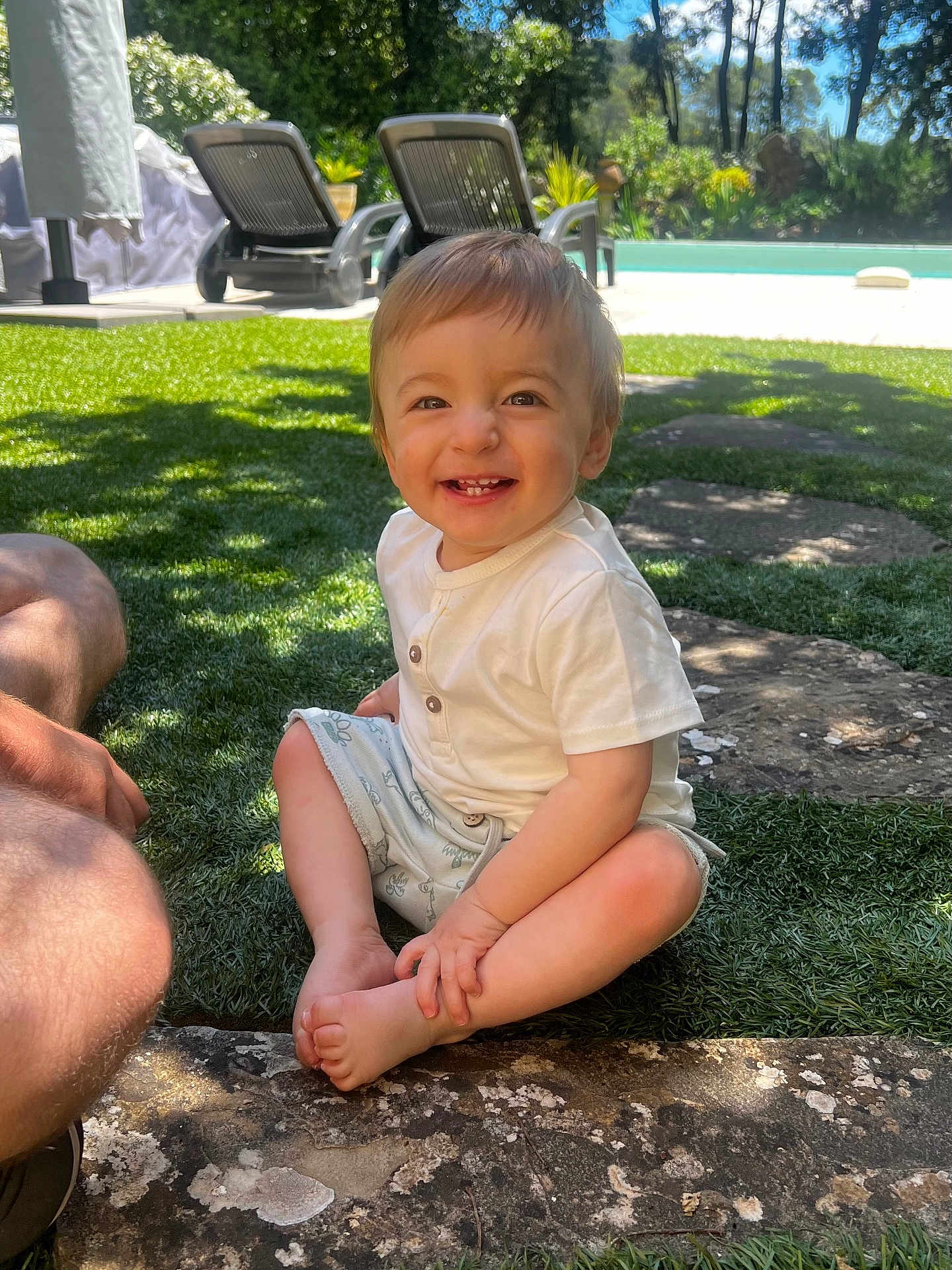 Maylone participe au concours pour gagner de l'argent avec cette photo : child, toddler, smiling, grass, outdoor, sunlight, pool, garden_chair, happy, barefoot, shorts, white_shirt, person, nature, summer, daytime, sitting, cute, playful, leisure