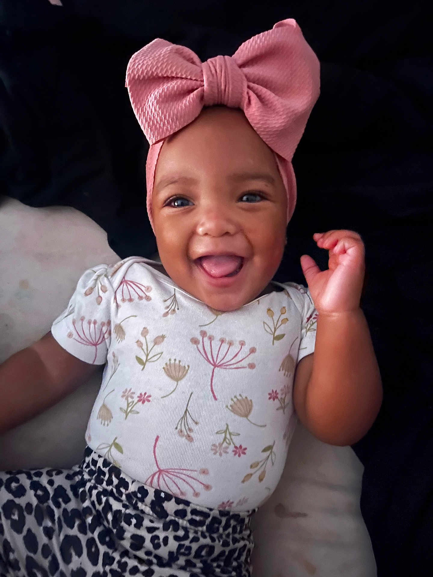 Katara joined the competition — help win amazing prizes! baby, child, smiling, headband, pink_bow, floral_shirt, leopard_print, tongue_out, happy, cute, portrait, infant, clothing, lying_down, dark_background, closeup, person, baby_fashion, playful, adorable