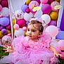 toddler, pink_dress, grass, balloons, butterfly_decorations, headpiece, child, outdoor, cute, playful, sitting, portrait, celebration, festive, flower_decorations, white_tights, happy, event, colorful, innocence