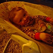 Lillian is registered to the contest to win money with this photo: baby, infant, baby_rocker, leopard_print, carpet, smile, child, indoor, seat, toy, clothing, person, blur, low_light, happy, young_child, baby_toys, seat_belt, face, furniture
