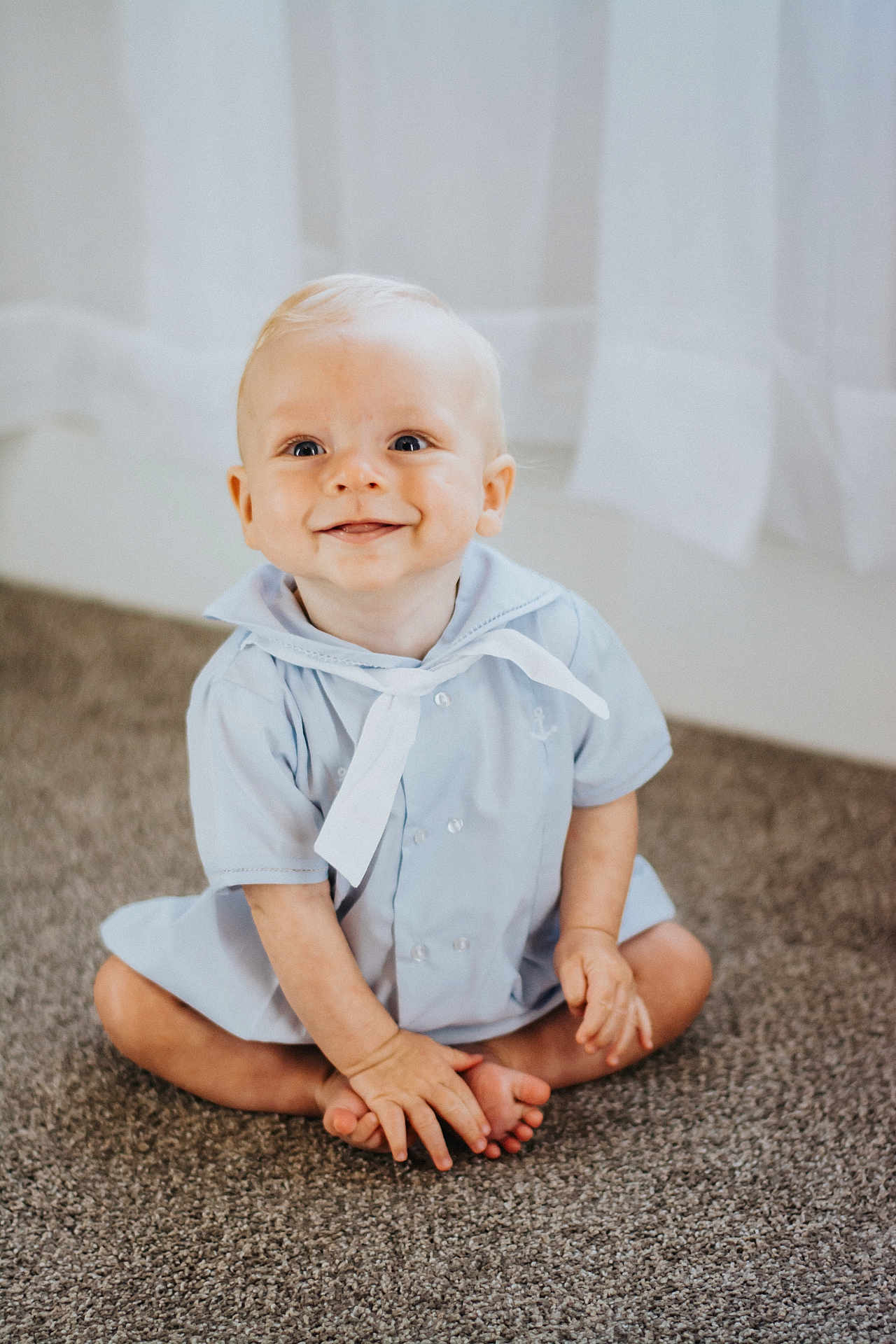 Ryatt is registered to the contest to win money with this photo: baby, child, smiling, sitting, carpet, blue_clothing, sailor_outfit, indoor, cute, happy, face, hands, feet, blond_hair, infant, portrait, young_child, person, floor, curtains