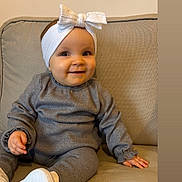 Andréa participe au concours pour gagner de l'argent avec cette photo : baby, infant, child, headband, bow, smile, sitting, couch, sofa, grey_outfit, white_shoes, indoor, portrait, cute, happy, one_person, hands, feet, cozy, soft_tones