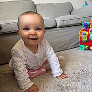 Andréa a rejoint le concours — aidez-le/la à gagner de superbes lots ! baby, infant, smiling, crawling, carpet, rug, sofa, living_room, toy, colorful_toy, knitted_cardigan, striped_pants, hands, eyes, face, indoor, flooring, cheerful, portrait, household