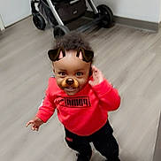 Titan joined the competition — help win amazing prizes! toddler, child, indoors, floor, red_clothing, puma_logo, dog_filter, face_filter, standing, stroller, toy, black_pants, black_shoes, curly_hair, playful, smiling, person, casual_wear, home, flooring
