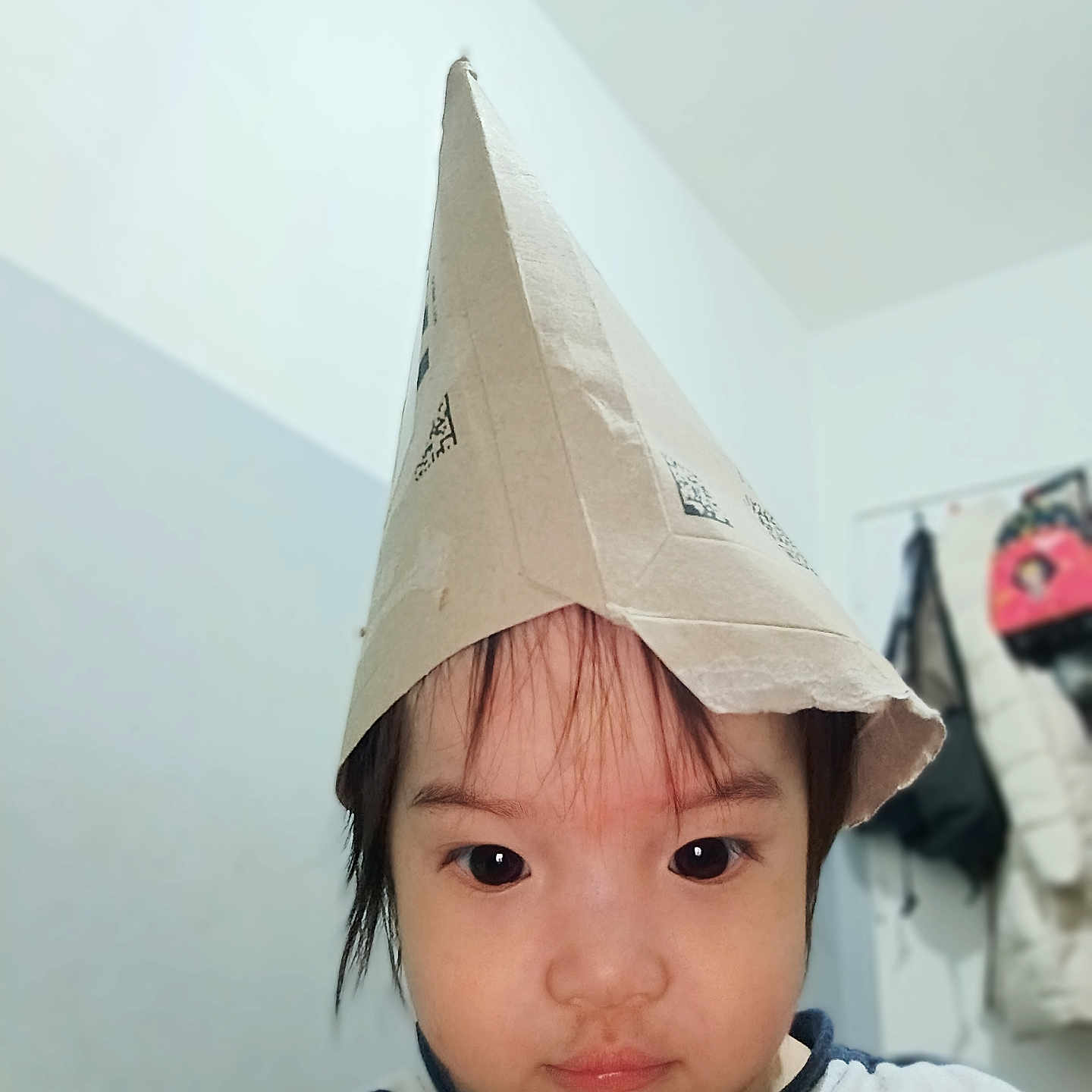 Aëlyss participe au concours pour gagner de l'argent avec cette photo : black_hair, bucket, casual, child, closeup, clothing, coats, curious, expression, face, headwear, indoor, paper_hat, person, playful, portrait, room, striped_shirt, toddler, young_child