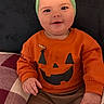 Kehlani is registered to the contest to win money with this photo: baby, child, infant, portrait, smiling, happy, sitting, indoors, halloween, pumpkin, costume, orange_shirt, green_headband, bow, jack_o_lantern, chair, cushion, home, face, photography