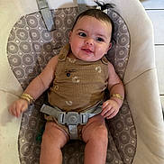Kehlani is registered to the contest to win money with this photo: baby, child, infant, smiling, portrait, sitting, bouncer, baby_chair, harness, patterned_fabric, indoor, home, brown_outfit, hair_bow, ponytail, bracelets, socks, happy, face, furniture
