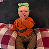 Kehlani is registered to the contest to win money with this photo: baby, child, infant, portrait, smiling, sitting, indoors, couch, cushion, plaid, pumpkin, halloween, orange_shirt, green_headband, bow, barefoot, hand_to_mouth, cozy, home_decor, facial_expression