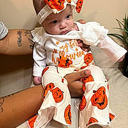 Mia joined the competition — help win amazing prizes! baby, child, infant, portrait, halloween, pumpkin, costume, bow, headband, white_clothing, orange, jack_o_lantern, sitting, held, adult_arms, indoor, plant, couch, facial_expression, photography