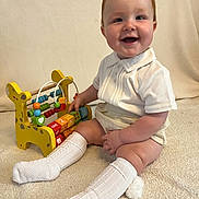 Jaxon is registered to the contest to win money with this photo: baby, child, smiling, toy, giraffe, abacus, carpet, white_clothing, knee_socks, indoor, cute, playful, happy, sitting, toddler, wooden_toy, colorful, person, face, infant