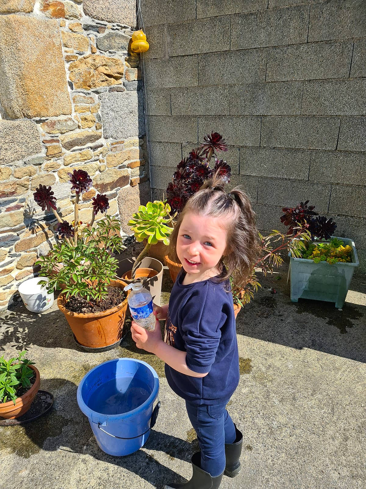 Maïna a rejoint le concours — aidez-le/la à gagner de superbes lots ! annual_plant, blue, brick, brickwork, bucket, cobblestone, electric_blue, flower, flowerpot, garden, grass, houseplant, joy, landscape, landscaping, person, plant, shrub, smile, soil