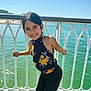 beachwear, blouse, child, clothing, face, female, fence, girl, happy, head, outdoors, pants, person, photography, portrait, railing, smile, summer, water, waterfront