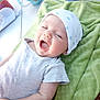 Leo is registered to the contest to win money with this photo: baby, infant, blanket, hat, smiling, yawning, white_clothing, green_blanket, table, mug, cup, soft_texture, relaxing, indoor, person, face, headwear, happy, child, cozy