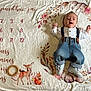 baby, infant, child, milestone_blanket, blanket, floral_pattern, numbers, calendar, wooden_ring, wooden_toy, suspenders, denim_jeans, shoes, smiling, lying_down, cute, nursery, white_background, decorative_art, portrait