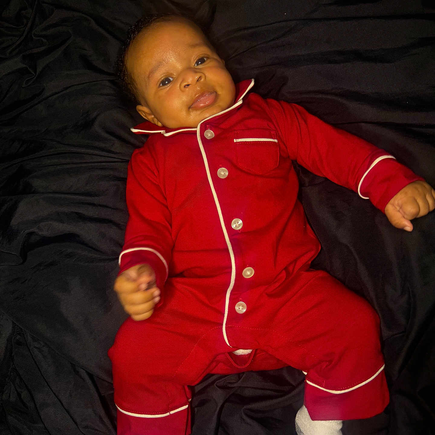 Tamaj joined the competition — help win amazing prizes! baby, infant, red_onesie, smile, lying_down, socks, dark_background, cute, child, portrait, happy, young, face, person, cozy, indoors, sleepwear, pajamas, small_hands, bright_colors