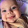 baby, face, tongue, smile, close_up, infant, child, cute, happy, clothing, bear_design, strap, eyes, cheeks, soft_background, indoors, person, young_child, cozy, portrait