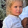 background, belt, blonde_hair, casual, child, clothing, curly_hair, face, flower, hand, holding, navy_pants, outdoor, person, portrait, serious_expression, skin, standing, white_shirt, young