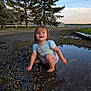 Oaklynn joined the competition — help win amazing prizes! toddler, child, muddy_puddle, water, gravel, splashing, smiling, outdoor, nature, trees, grass, dog, sky, clouds, dirt, barefoot, casual_clothing, playful, daytime, sunset
