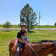 Oaklynn is registered to the contest to win money with this photo: adult, child, horse, helmet, glasses, grass, tree, fence, rope, outdoor, sunny, field, riding, nature, smile, person, animal, daylight, leisure, family