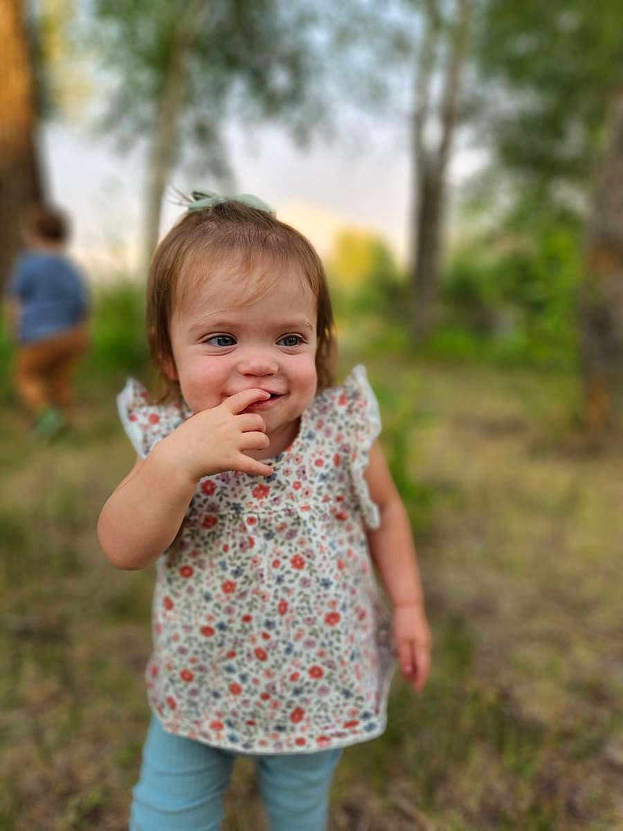 Oaklynn joined the competition — help win amazing prizes! toddler, child, outdoor, nature, grass, trees, floral_top, blue_pants, finger_in_mouth, curious, playful, person, young_child, blurry_background, daylight, greenery, casual_clothing, cute, smiling, two_children