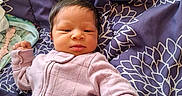 Rain is registered to the contest to win money with this photo: baby, newborn, infant, onesie, blanket, purple, pattern, floral, sleepwear, face, person, cute, small, child, lying_down, indoors, resting, fist, curious, soft