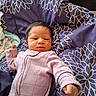 baby, newborn, infant, onesie, blanket, purple, pattern, floral, sleepwear, face, person, cute, small, child, lying_down, indoors, resting, fist, curious, soft
