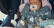 Rain is registered to the contest to win money with this photo: baby, infant, car_seat, pacifier, blanket, bottle, clothing, onesie, pink, gray, floral_pattern, sleepwear, child, newborn, face, person, indoors, resting, cute, cozy