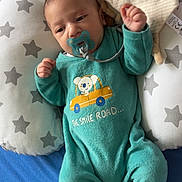 Raphaël participe au concours pour gagner de l'argent avec cette photo : baby, pacifier, onesie, pillow, star_pattern, blue_bed, infant, child, sleepwear, toy, cute, lying_down, cozy, soft_toy, face, hand, footed_pajamas, expression, indoors, comfort