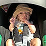 baby, car_seat, hat, harness, infant, child, sunlight, seat, safety, clothing, person, skin, legs, feet, cute, outdoor, expression, headwear, strap, infant_care