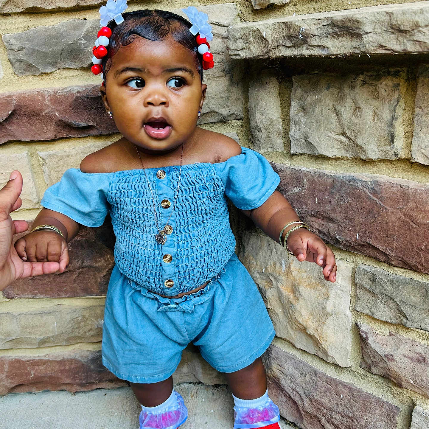 Samauni joined the competition — help win amazing prizes! blue_outfit, bracelets, casual_wear, child, colorful, curious_expression, cute, fashion, hair_accessories, hand_holding, necklace, outdoor, person, portrait, red_shoes, sidewalk, standing, stone_wall, toddler, young_child