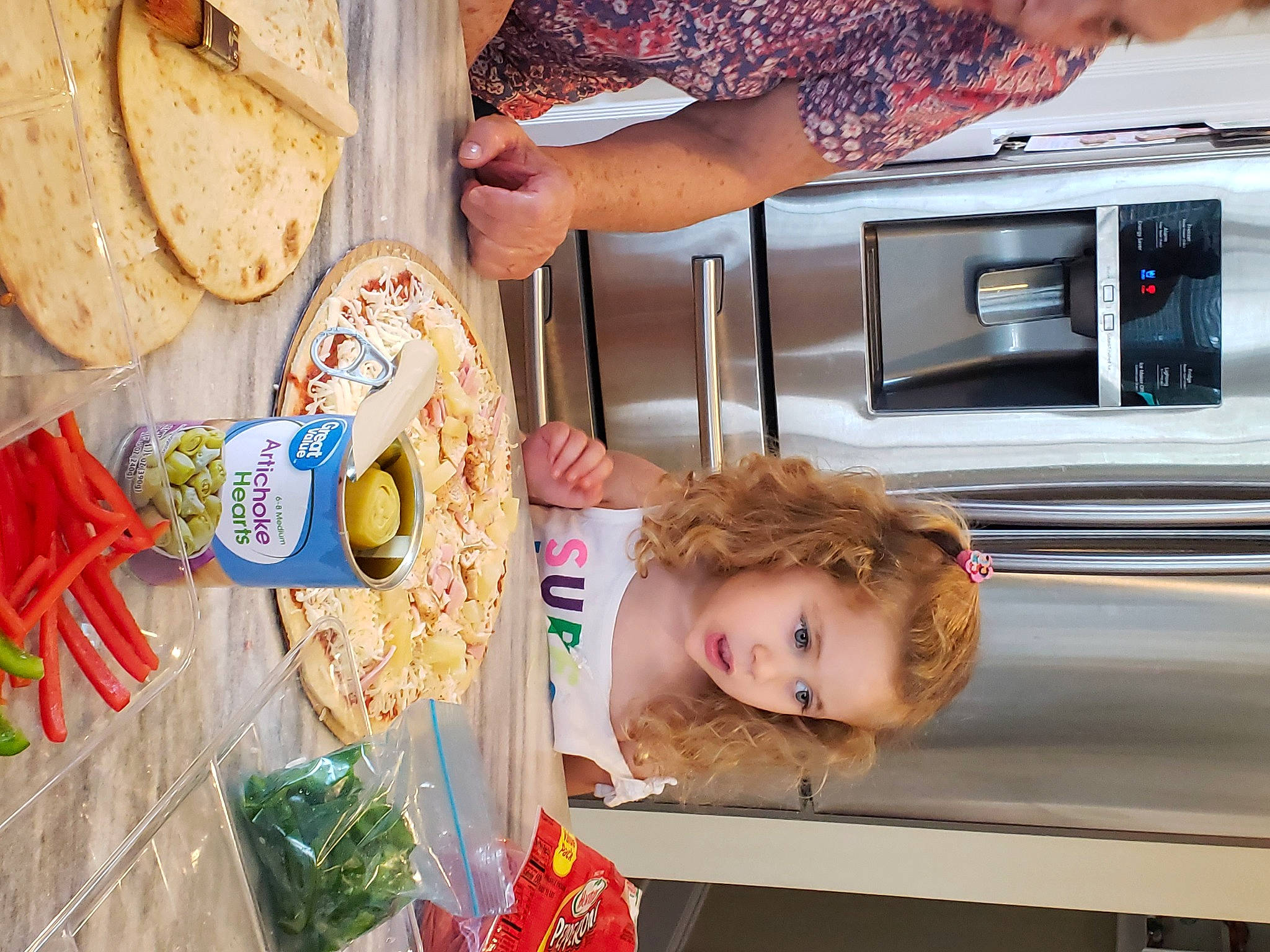 Alicia is registered to the contest to win money with this photo: chapati, child, cooking, cuisine, food, fun, home_appliance, kitchen, kitchen_appliance, major_appliance, microwave_oven, person, plate, refrigerator, room, roti, t_shirt, tableware, toddler, wood