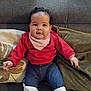 baby, child, infant, sitting, couch, red_sweater, denim_pants, white_booties, curly_hair, face, smile, indoors, pillow, blanket, cozy, cute, portrait, young_child, comfortable, happy