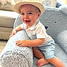 baby, child, boy, hat, straw_hat, smiling, happy, blue_shorts, white_shirt, armchair, furniture, indoor, cozy, cute, portrait, person, infant, soft_texture, living_room, playful