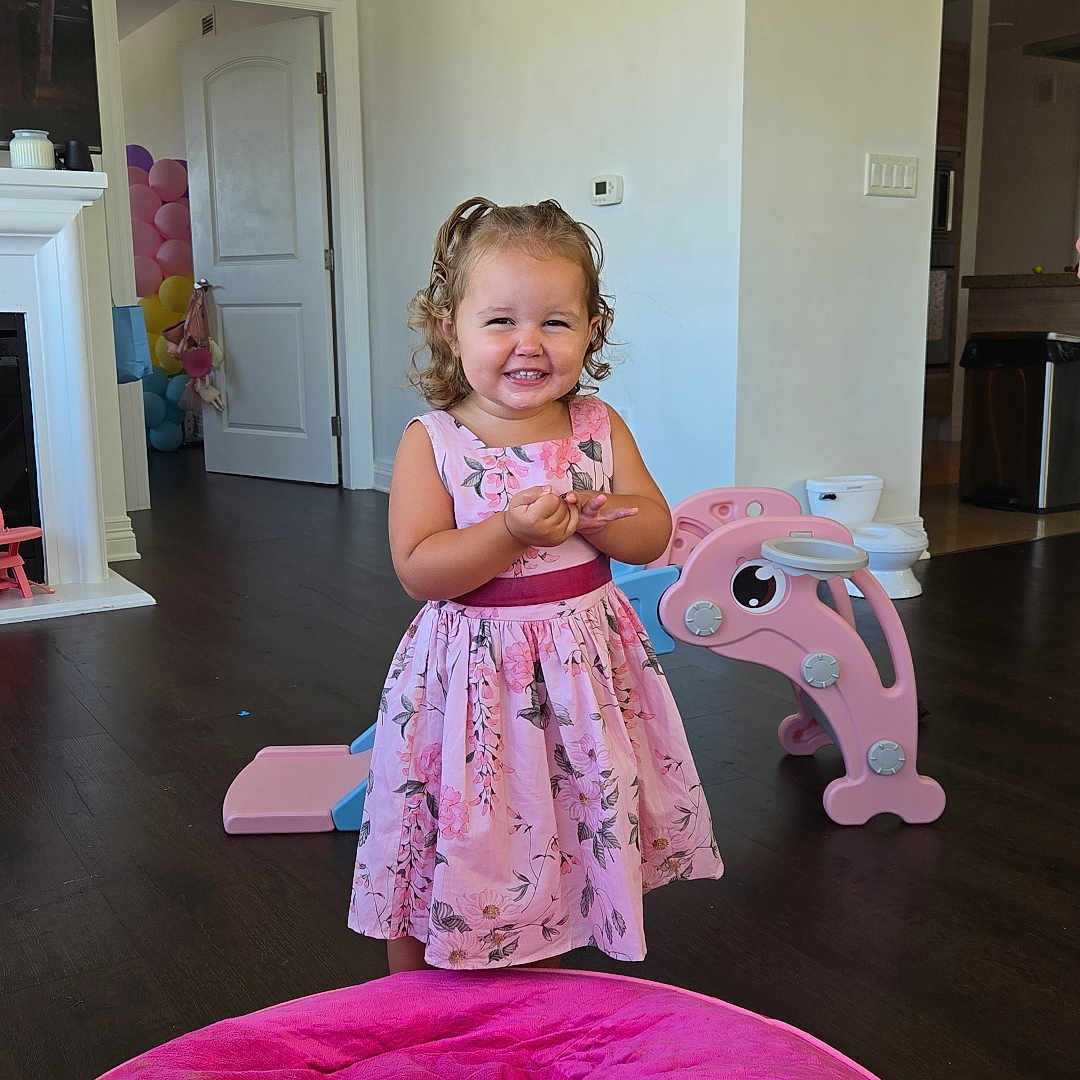 Perla joined the competition — help win amazing prizes! beanbag, child, curly_hair, dolphin, door, dress, flooring, floral, indoor, light_switch, living_room, pink, polka_dot, red_bow, slide, smiling, thermostat, toddler, toy, wall