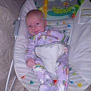 Angel is registered to the contest to win money with this photo: baby, infant, unicorn_pajamas, baby_rocker, animal_illustrations, giraffe, crocodile, bird, monkey, purple_clothing, smiling, cute, indoor, quilted_blanket, sock, child, face, seated, soft_toys, colorful