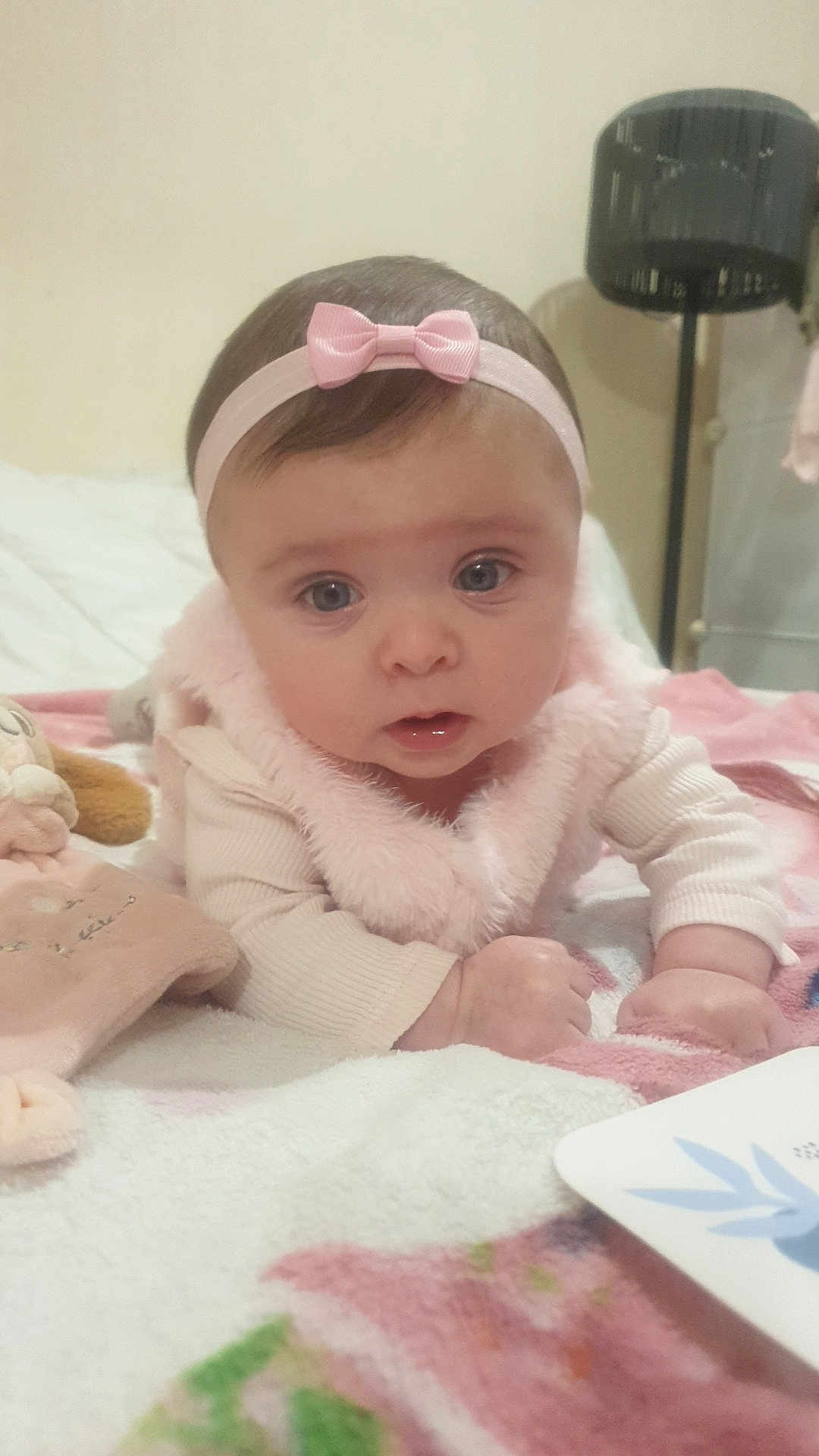 Amélia participe au concours pour gagner de l'argent avec cette photo : baby, infant, headband, pink, blanket, soft_toy, indoor, curious, clothing, face, hands, lying_down, toddler, child, portrait, cute, cozy, bed, furniture, expression