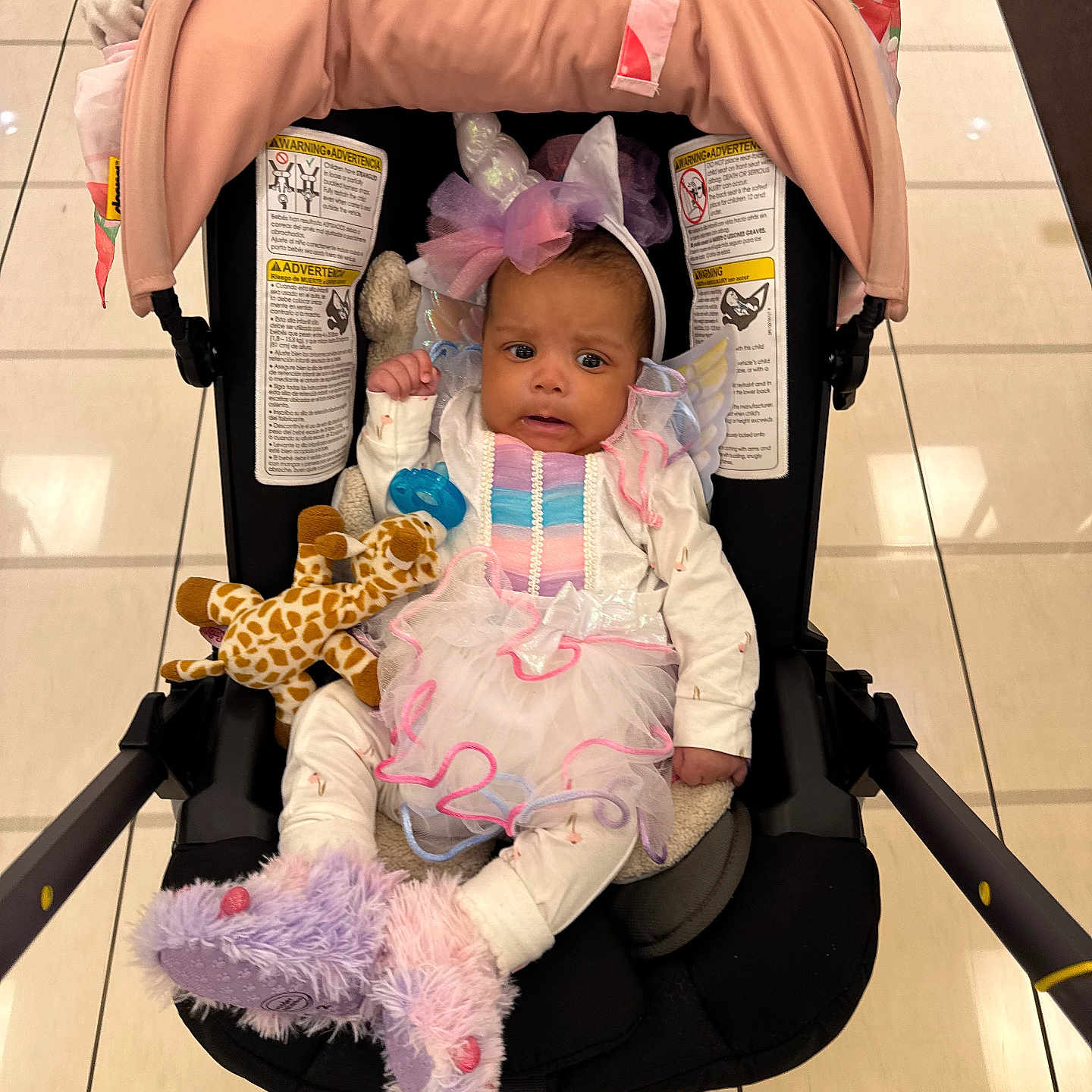 Kali J joined the competition — help win amazing prizes! baby, child, clothing, cute, floor_tiles, giraffe, headband, indoor, infant, person, pink, plush_toy, portrait, purple, slippers, stroller, toy, unicorn_costume, white, wings