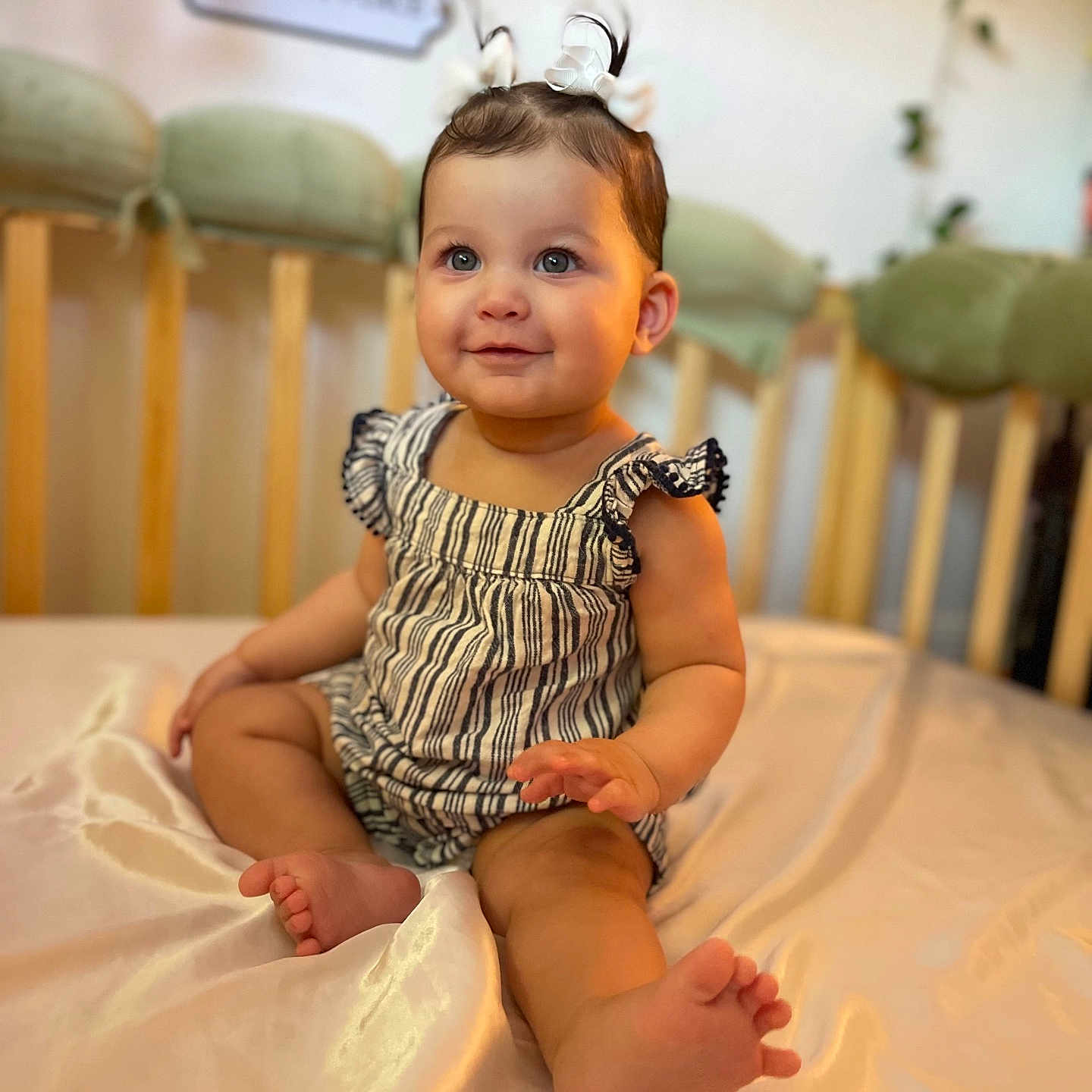 Sofia is registered to the contest to win money with this photo: arm, baby, blanket, child, clothing, crib, cute, furniture, hair_bow, happy, indoors, infant, person, portrait, sitting, skin, smiling, soft_focus, toe, young
