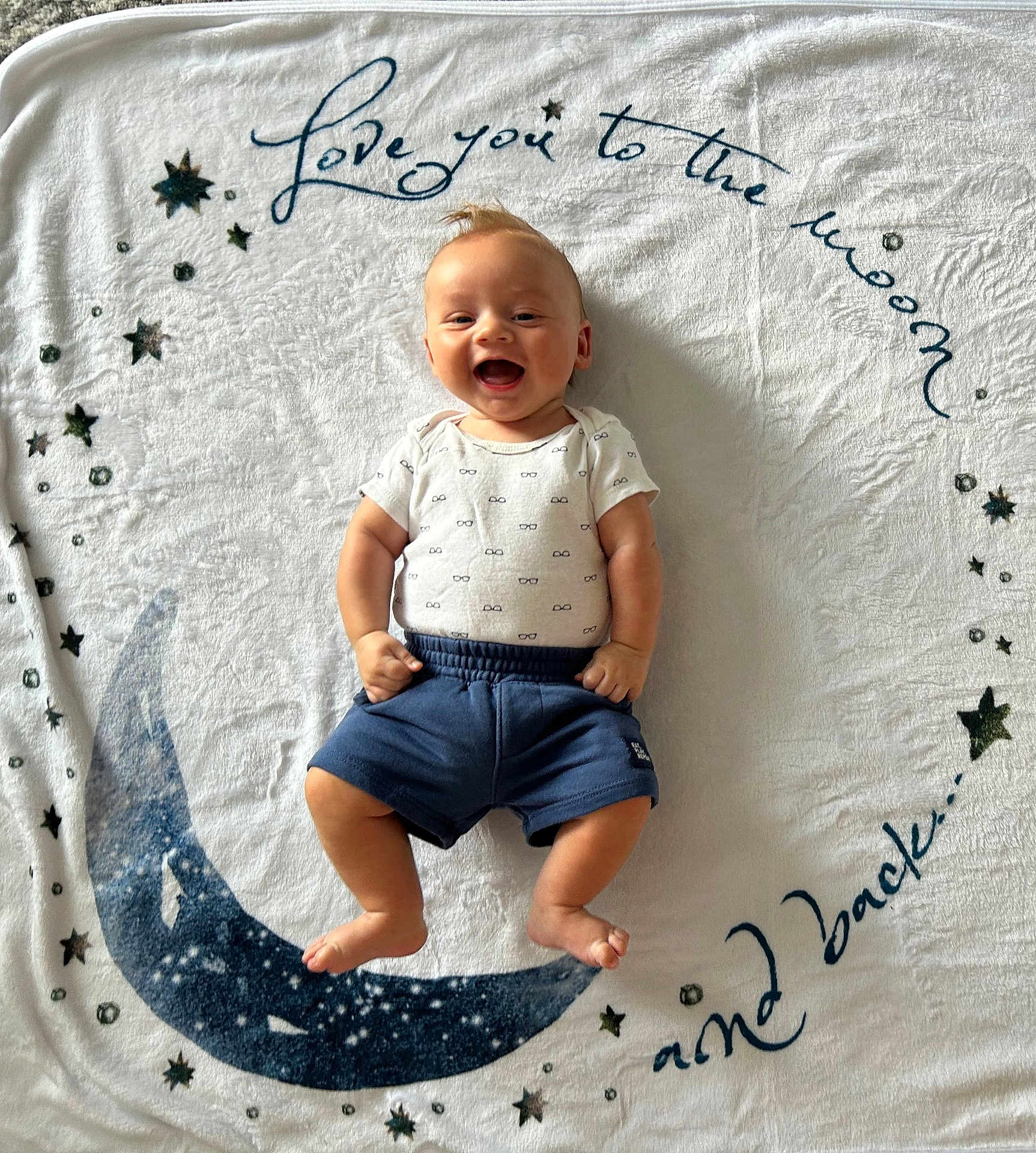 Carson joined the competition — help win amazing prizes! baby, blanket, smiling, infant, clothing, shorts, onesie, face, happy, lying_down, text, moon, stars, pattern, fabric, cute, child, portrait, indoor, baby_boy