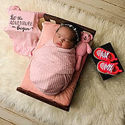 Riot is registered to the contest to win money with this photo: newborn, baby, swaddled, pink_blanket, wooden_bed, crocheted_teddy_bear, baby_sneakers, pink_onesie, text_on_clothing, fluffy_rug, cushion, sleeping, headband, floor, wooden_floor, indoor, soft_lighting, portrait, cozy, baby_clothing