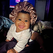 Isabella is registered to the contest to win money with this photo: baby, blanket, bonnet, child, clothing, crawling, cute, expression, eyes, face, happy, headwear, indoors, infant, person, portrait, satin, smile, toy, warm_lighting