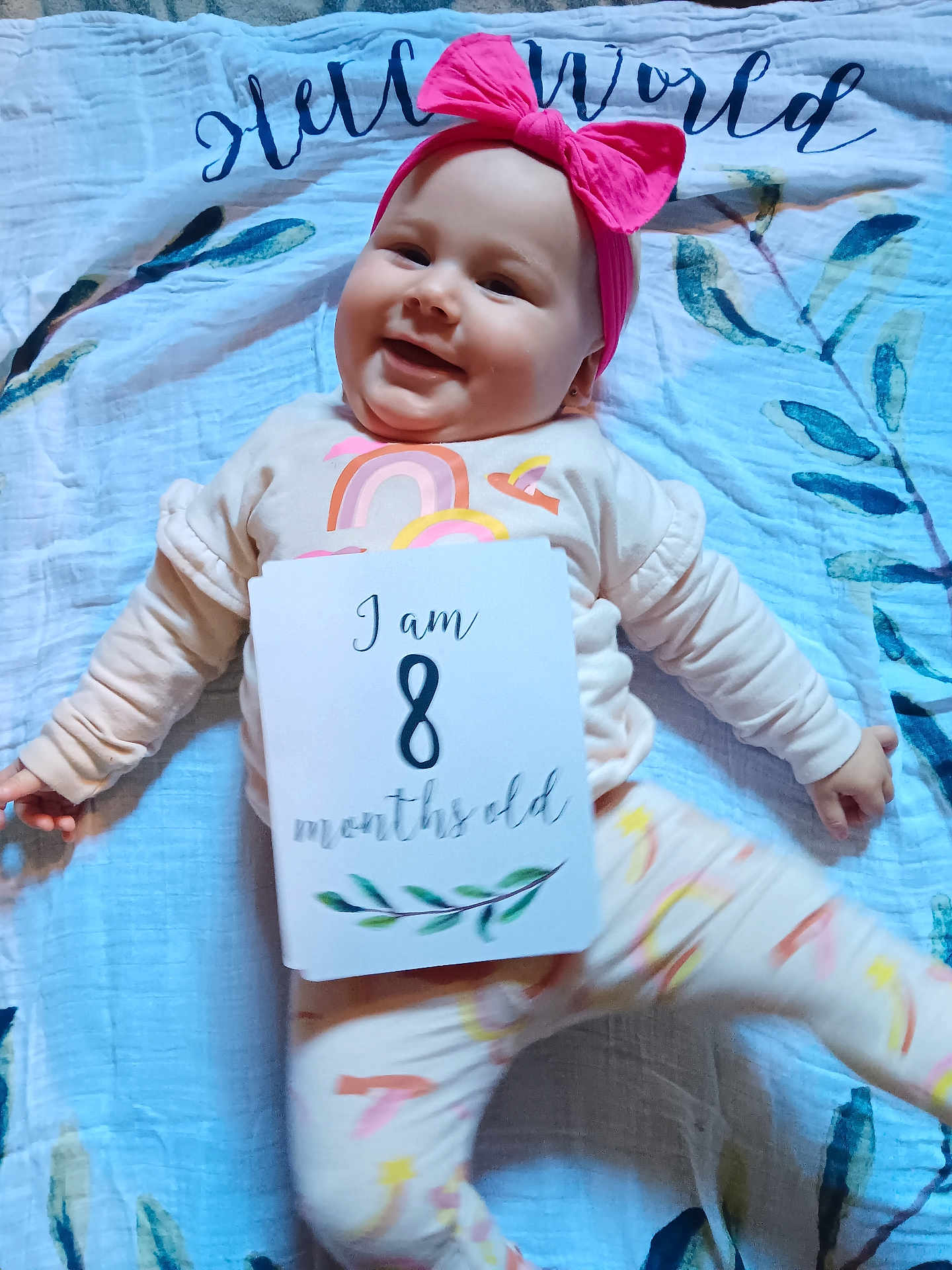 Stevie joined the competition — help win amazing prizes! baby, infant, smiling, pink_bow, headband, blanket, pajamas, rainbow, sign, eight_months_old, lying_down, cute, happy, child, face, clothing, indoor, person, pattern, soft