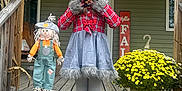 Madeline is registered to the contest to win money with this photo: child, costume, wolf, porch, pumpkin, scarecrow, flowers, fall, seasonal_decoration, smile, wooden_steps, outdoor, plaid, gray_clothing, festive, holiday, yellow_flowers, happy, person, decor