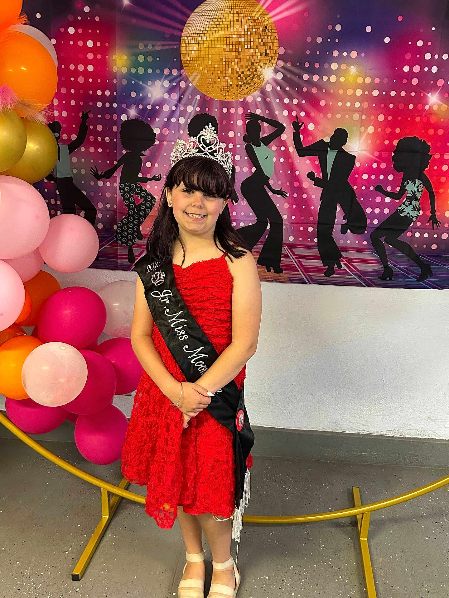 Madeline joined the competition — help win amazing prizes! child, girl, red_dress, tiara, sash, balloons, disco_ball, disco_theme, party, celebration, smile, indoor, portrait, decorations, floor, wall, happy, event, festive, background