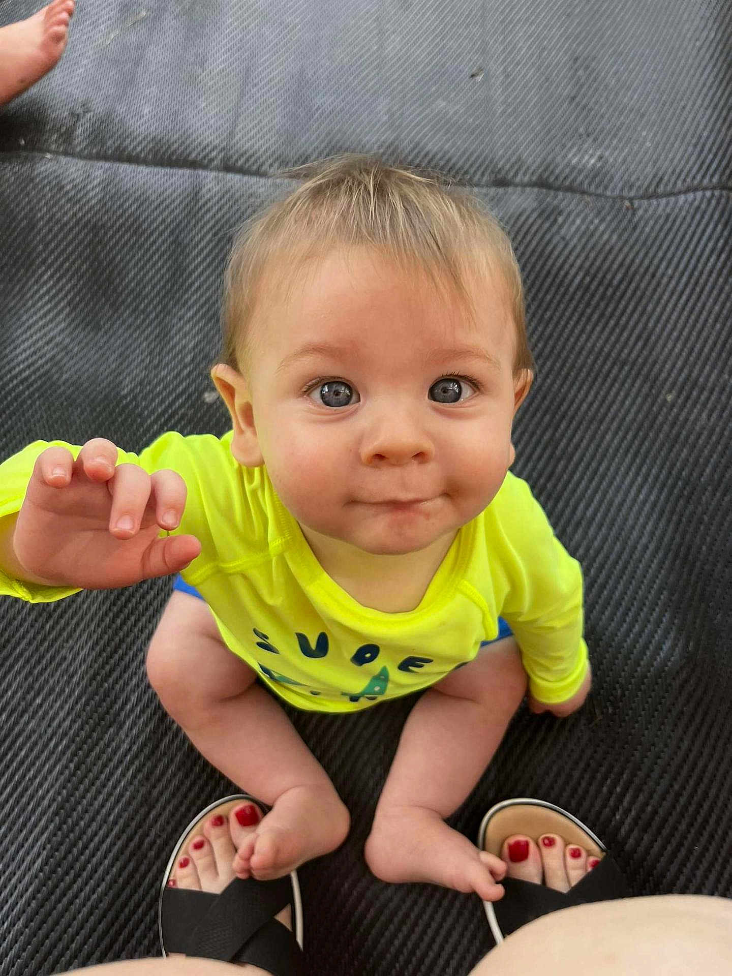 Lincoln is registered to the contest to win money with this photo: baby, child, infant, yellow_shirt, blue_shorts, barefoot, toes, red_nail_polish, feet, playful, curious, sitting, mat, texture, indoors, portrait, face, hand, eyes, expression